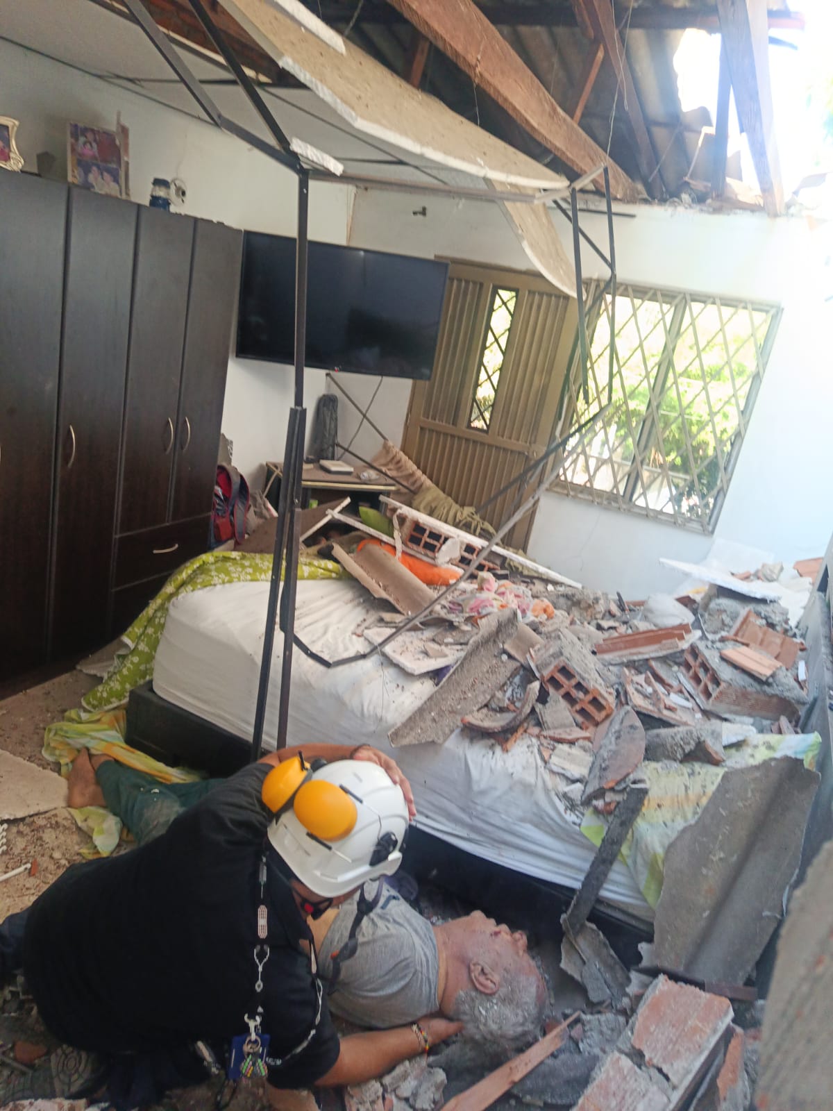 An emergency responder assists an injured resident inside a damaged home.