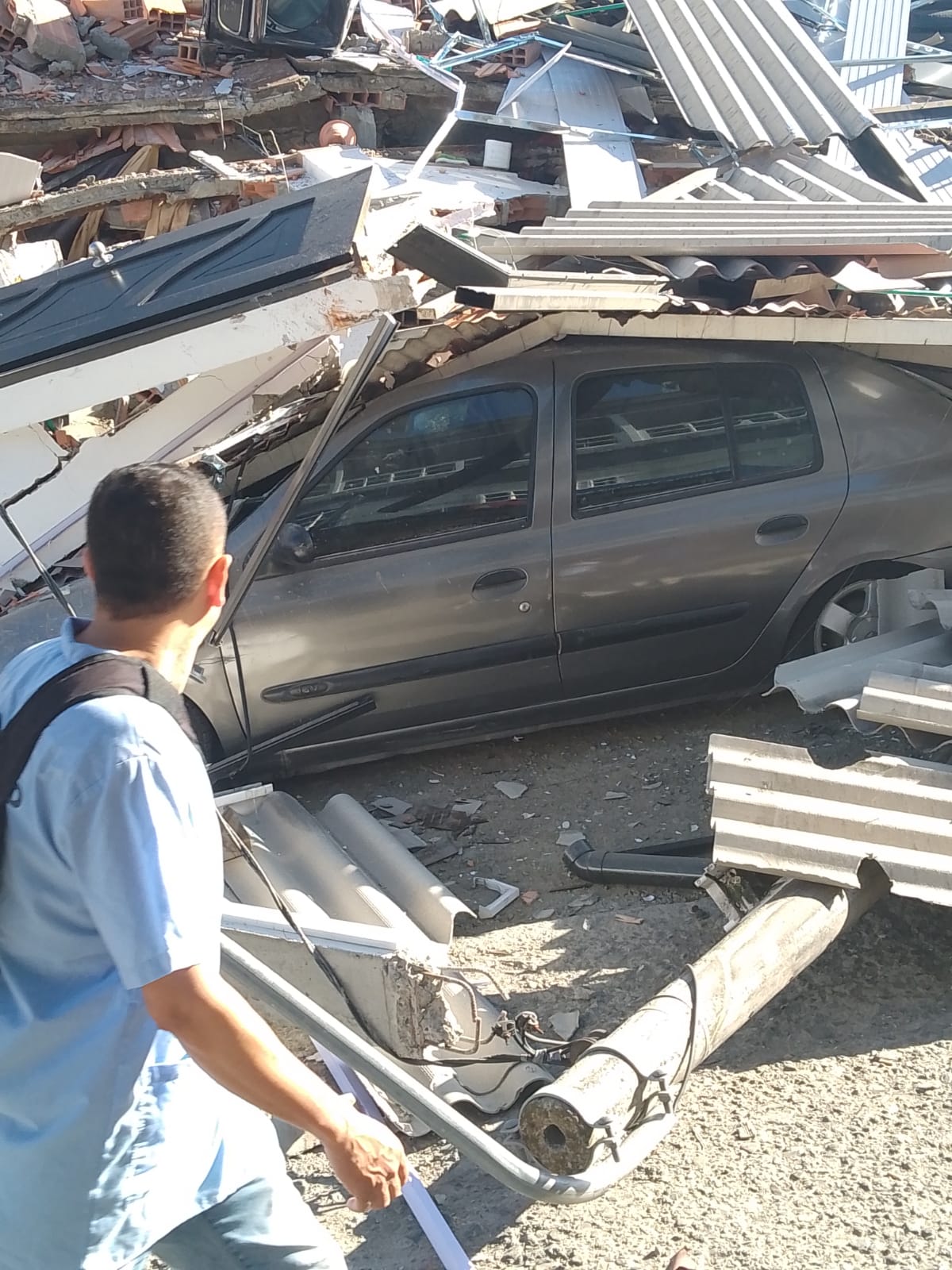 A vehicle trapped beneath collapsed roofing and construction materials.